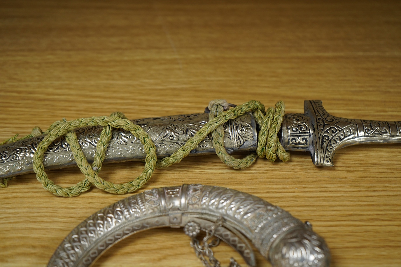 An Omani silver spice box in the form of a curved powder flask, together with a Moroccan dagger Jambiya with nickel hilt and sheath, both 20th century. Condition - fair.